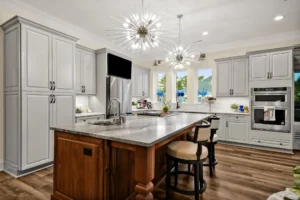 Modern gray kitchen with wood island, starburst chandeliers, stainless appliances, and natural light.