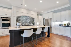 Modern white kitchen with dark island, wood floors, and geometric backsplash.