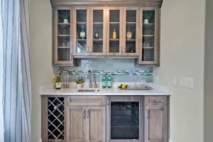 Stylish modern home bar with light wood cabinets, quartz countertop, and glass-front storage.