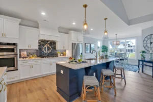 Bright modern kitchen with blue island, gold fixtures, white cabinets, and natural wood flooring.