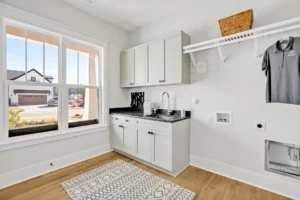Modern laundry room with white cabinets, wood floors, natural light, and sleek functional design.