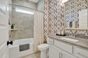 Modern bathroom with white vanity, granite countertop, and gold geometric wallpaper accents.