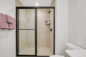 Modern bathroom with glass shower, matte black fixtures, beige tiles, and rose towels.