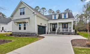 Modern farmhouse with gray siding, dark trim, front porch, dormer windows, and two-car garage.