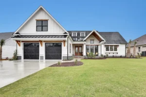 Modern white farmhouse with black trim, wood accents, two-car garage, and lush green lawn.