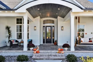 Modern farmhouse front porch with white columns, glass doors, and cozy fall decorations.