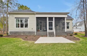 Rear exterior of modern single-story home with screened porch, brick foundation, and green lawn.