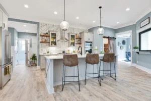 Modern white kitchen with wood shelves, leather stools, and stainless steel appliances.