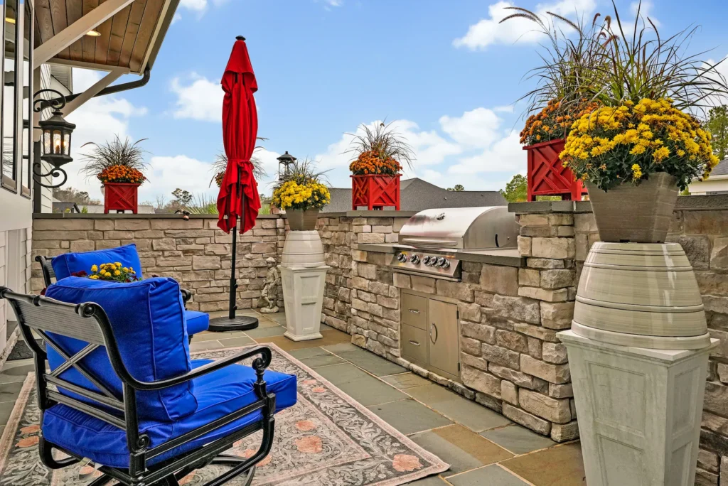 Modern patio with blue chairs, red umbrella, stone wall, and built-in stainless steel grill.