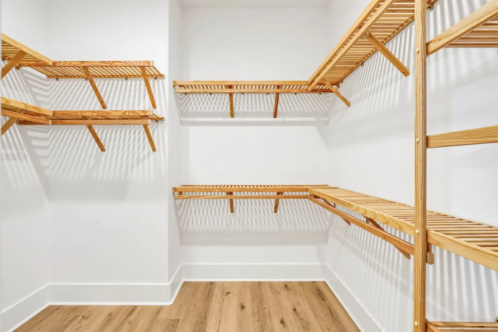Modern walk-in closet with light wood shelves, white walls, and minimalist organized design.