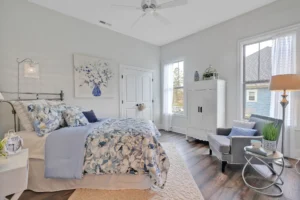 Calm blue and gray bedroom with floral bedding, white furniture, and natural light.