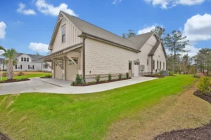 Modern beige Craftsman-style suburban home with dark roof, paved driveway, and manicured green lawn.