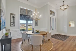 Elegant dining room with round wooden table, beige chairs, chandelier, and warm neutral decor.