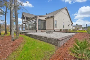 Modern beige lakeview home with screened porch, stone patio, and elegant landscaped yard.