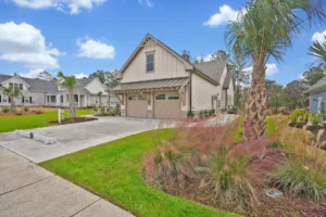 Modern beige suburban home with green lawn, palm trees, and wood-accented garage under blue sky.