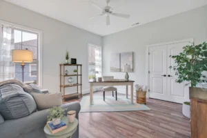 Bright minimalist home office with natural light, wooden desk, cozy seating, and indoor plants.
