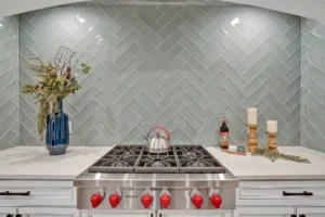 Modern kitchen with gray herringbone backsplash, stainless steel stove, white cabinets, and stylish decor.