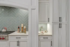 Elegant modern white kitchen with herringbone backsplash, black hardware, and stainless steel appliances.