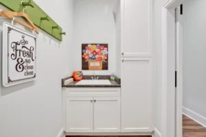 Modern white laundry room with green rack, dark countertop, and colorful wall art.