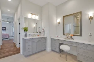 Modern master bathroom with white countertops, gray cabinets, and warm lighting near adjoining bedroom.