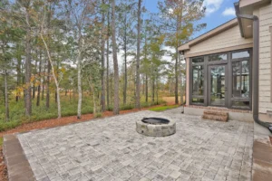 Spacious modern patio with stone fire pit and wooded backyard scenery.