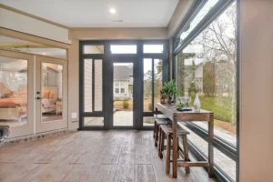Bright modern sunroom with glass walls, wood floors, and indoor plants overlooking lush greenery.
