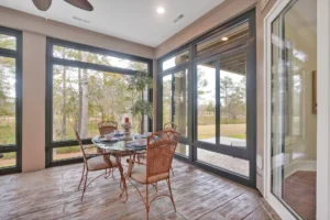 Bright sunroom with glass walls, rustic wood floors, and outdoor forest views.