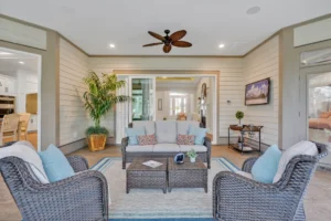 Coastal sunroom with wicker furniture, beige paneling, and natural light creating a relaxing atmosphere.