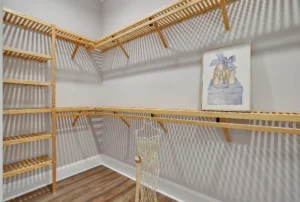 Spacious modern walk-in closet with light wood shelving, gray walls, and warm brown flooring.