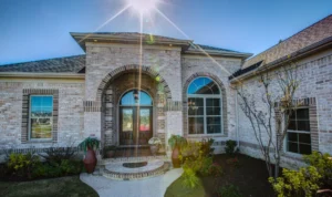 Elegant light brick home with arched entryway, dark wood doors, and sunny landscaped walkway.