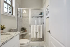 Bright modern bathroom with glass shower, granite countertop, white towels, and natural light.
