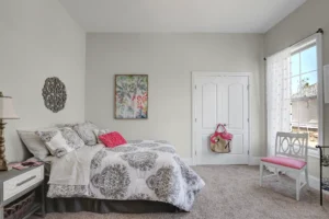 Bright neutral bedroom with pink accents, cozy bedding, and natural sunlight filtering through sheer curtains.