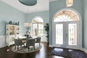 Bright airy dining room with soft blue walls, round table, and elegant glass double doors.