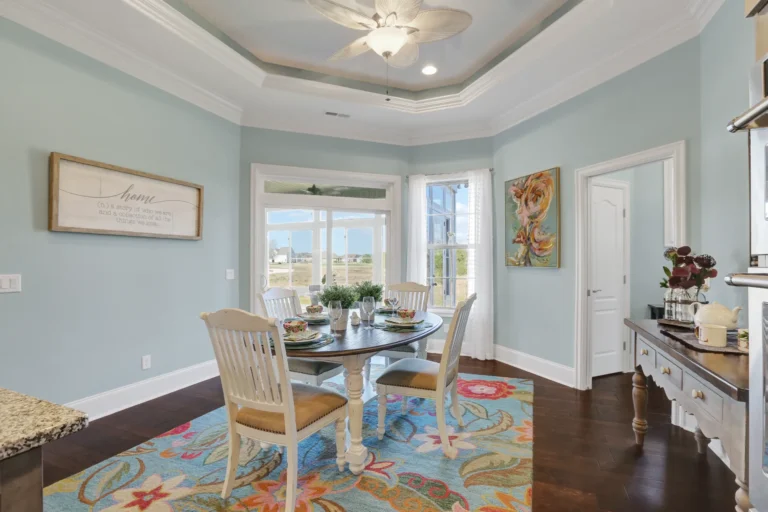 Coastal dining room with seafoam blue walls, wooden table, white chairs, and colorful floral rug.