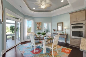 Coastal dining room with pastel blue walls, hardwood floors, and natural light through large windows.
