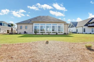 Rear view of modern single-story home with glass sunroom, brick exterior, and spacious backyard.