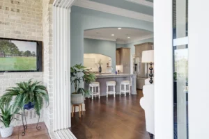 Modern open-concept living room and kitchen with light blue ceiling, white bar stools, and greenery.