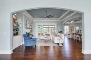 Bright coastal living room with soft blue walls, white furniture, and sunlit hardwood floors.