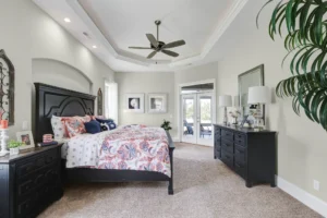 Spacious elegant bedroom with tray ceiling, dark wood furniture, and colorful cozy bedding.