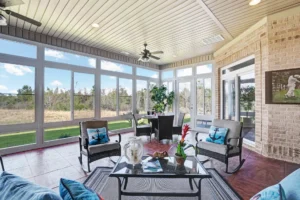Bright sunroom with wicker chairs, blue cushions, and natural light overlooking lush greenery.