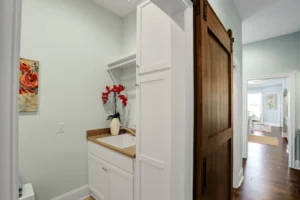 Bright modern farmhouse laundry room with white cabinets, wood countertop, and rustic sliding barn door.