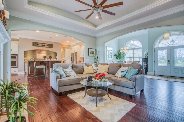 Modern open-concept living room with gray sectional, hardwood floors, natural light, and elegant kitchen view.