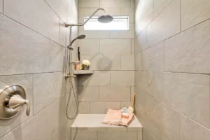 Modern beige and gray walk-in shower with bench, natural light, and spa-inspired decor.