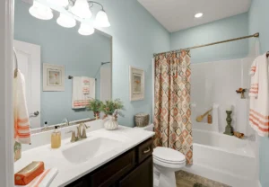 Modern light blue bathroom with dark wood vanity, white countertop, and warm orange décor accents.