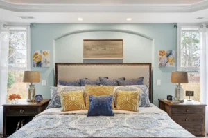 Modern bedroom with beige headboard, blue and yellow décor, soft aqua walls, and natural light.