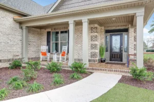 Modern brick home with white rocking chairs, orange cushions, and elegant front porch landscaping.