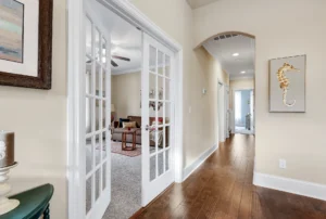 Warm hallway with hardwood floors, French doors, golden seahorse art, and arched entryway.