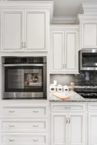Modern white kitchen with black backsplash, granite countertops, and built-in stainless steel appliances.
