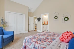 Cozy beige bedroom with paisley bedding, blue chair, and warm natural light.