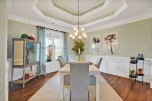 Elegant sage green dining room with chandelier, coffered ceiling, and gray upholstered chairs.